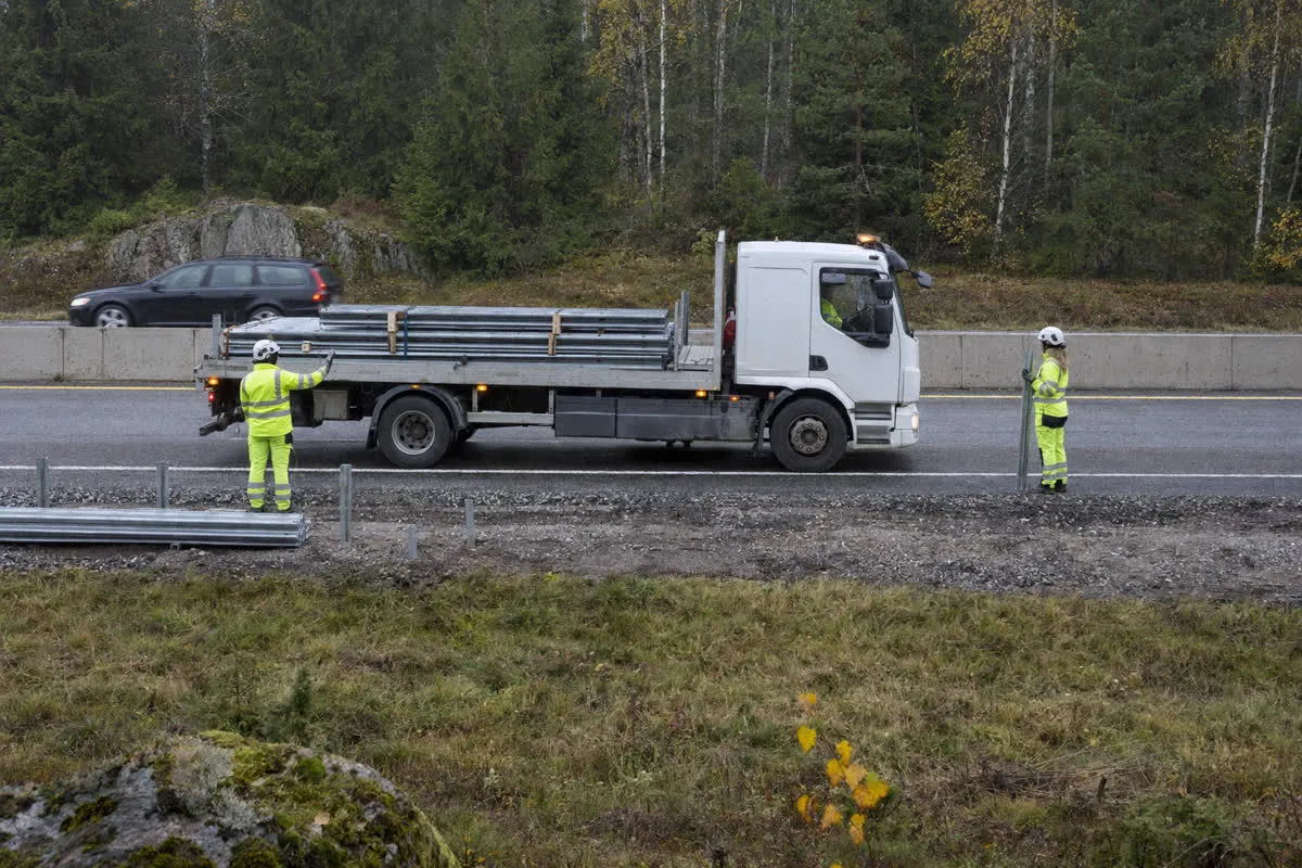 Lastbil med räckesbalkar står vid vägkanten medan vägarbetare väntar